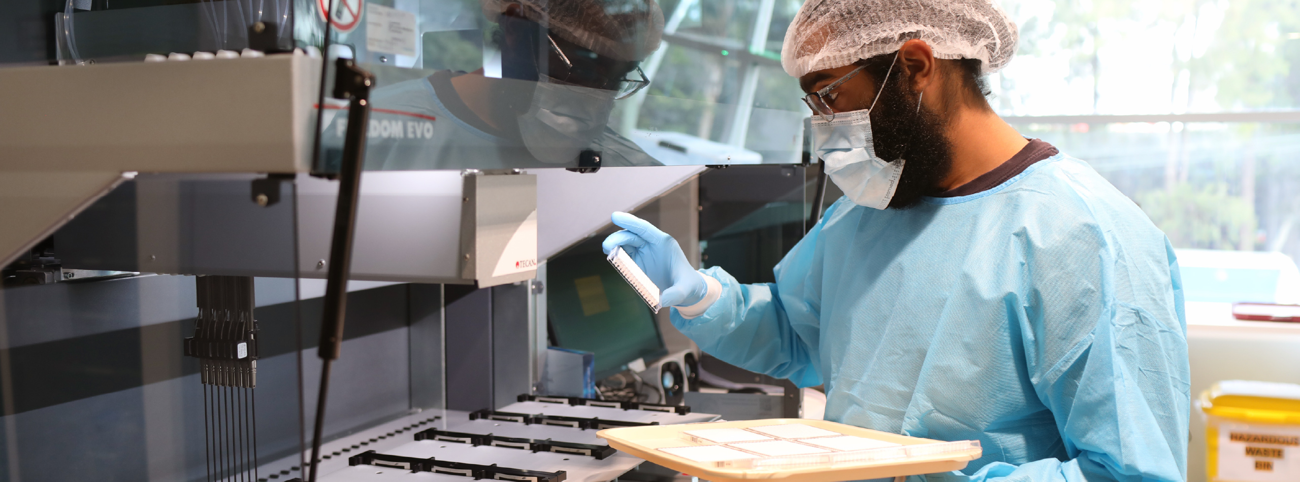 A man in a blue uniform operates a machine, focused on his task in a laboratory setting.