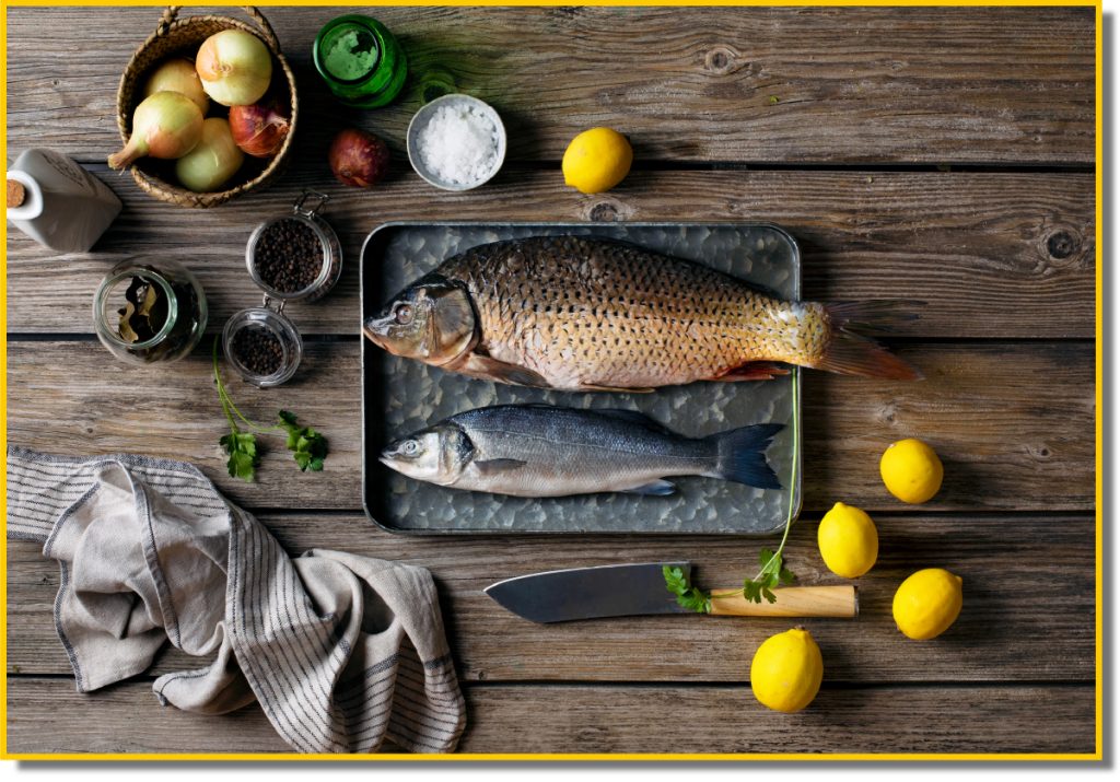 A fresh fish and sliced lemons arranged on a wooden table, showcasing a vibrant and appetising presentation.