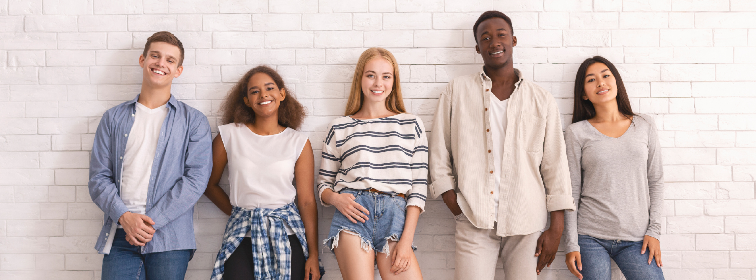 A group of young people poses together in front of a textured brick wall, smiling and enjoying each other's company.