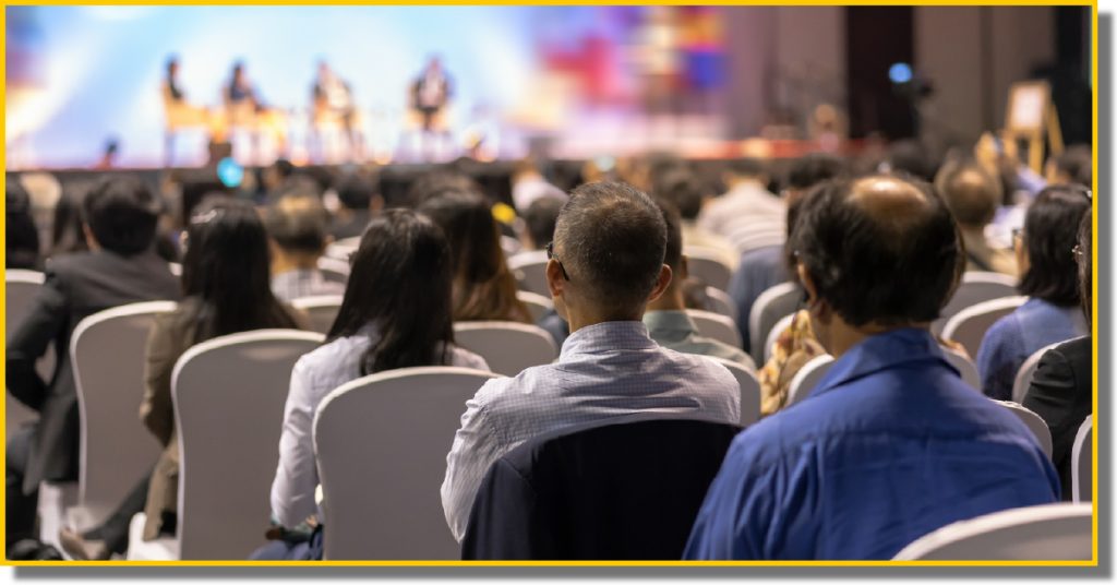 A large crowd of people seated in a conference room, engaged in discussions and presentations.