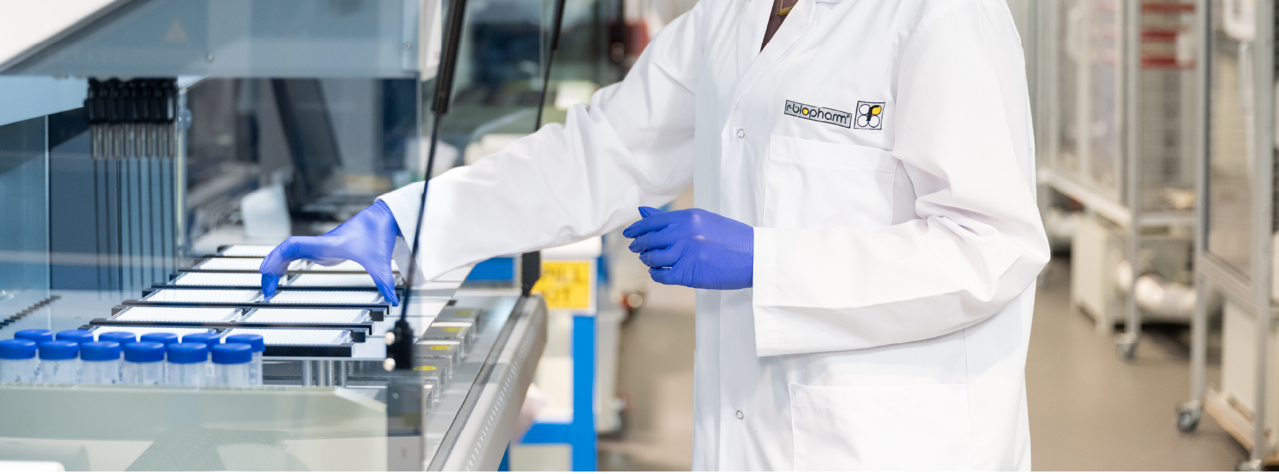 A woman in a lab coat operates a complex machine in a laboratory setting, focused on her task.