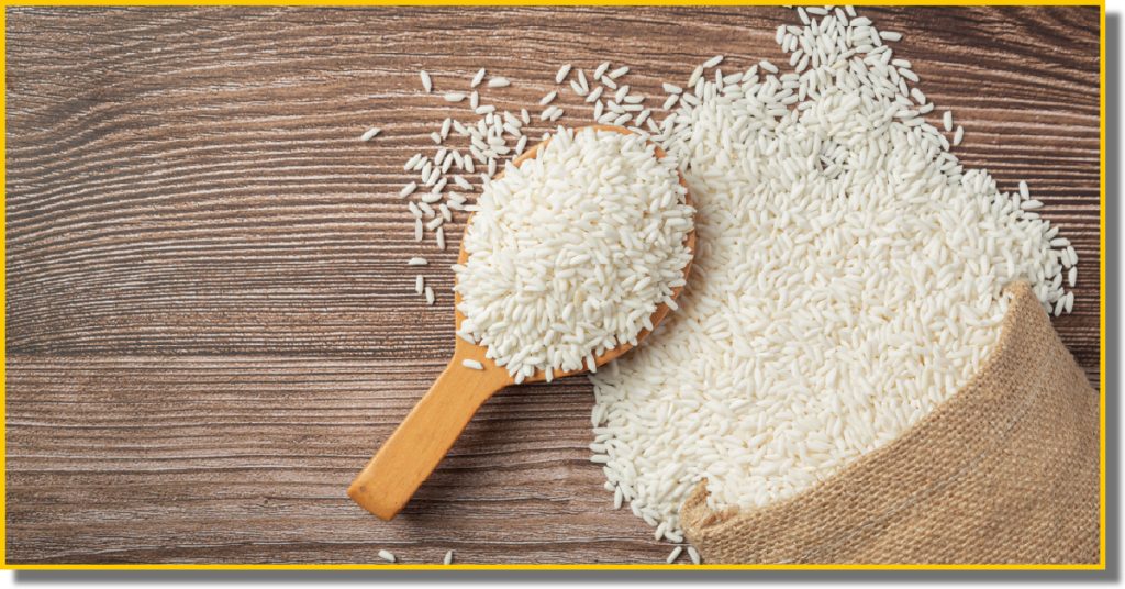 a sack of white rice poured onto a wooden table with a wooden spoon