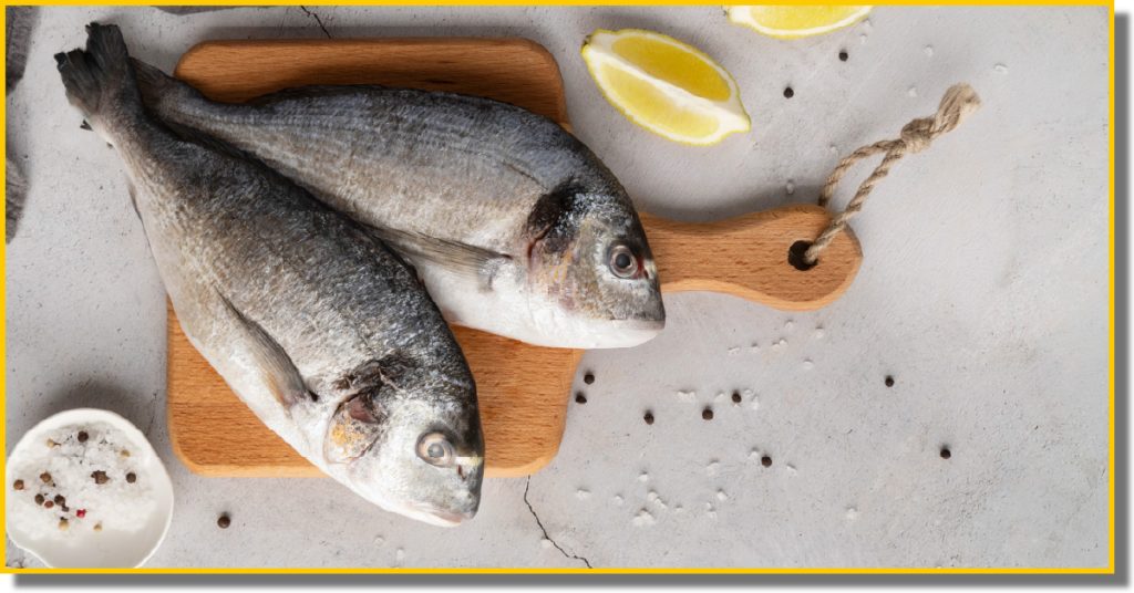Two fish on a wooden cutting board, accompanied by fresh lemon slices
