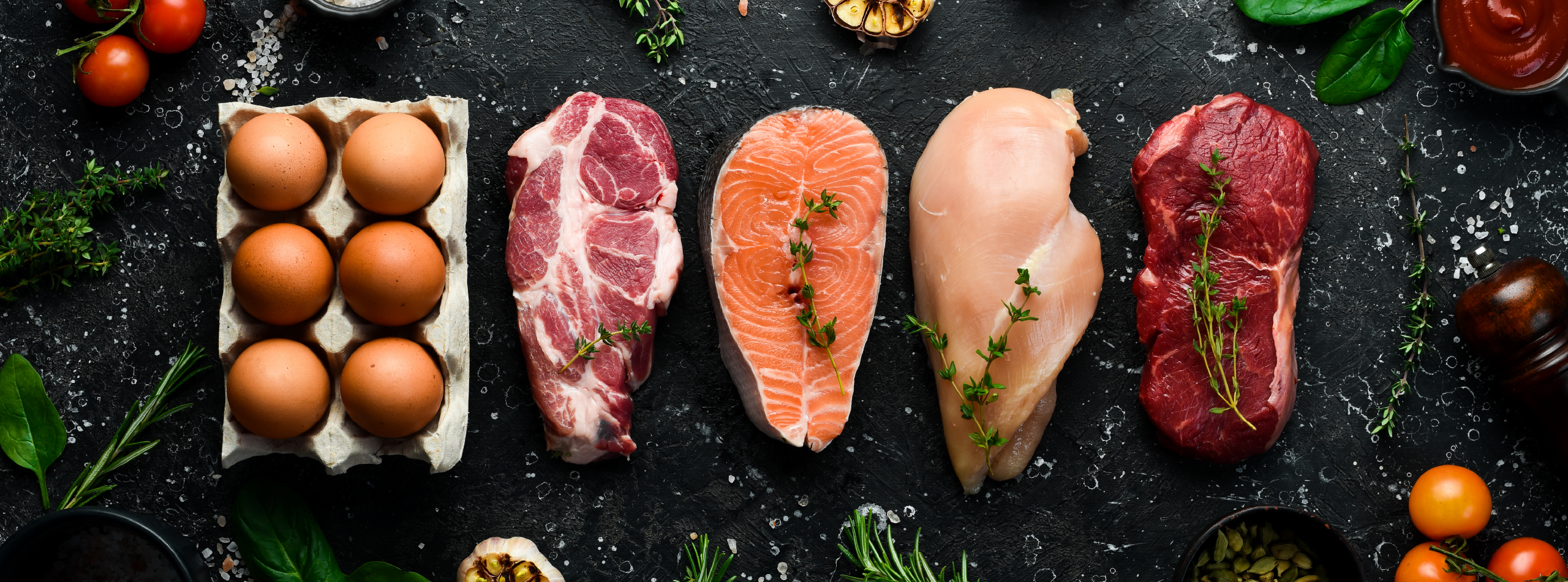 Raw meat, eggs, tomatoes, and fresh herbs arranged on a black background
