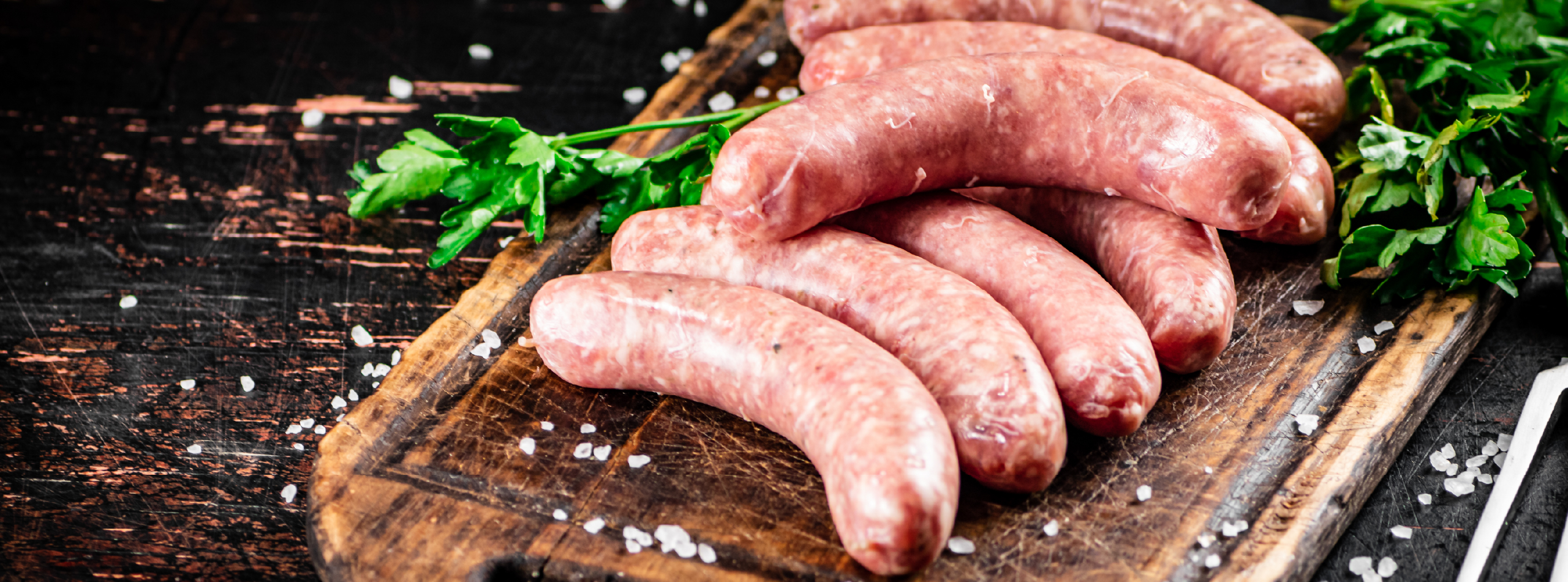 Raw sausages arranged on a wooden cutting board, garnished with fresh parsley