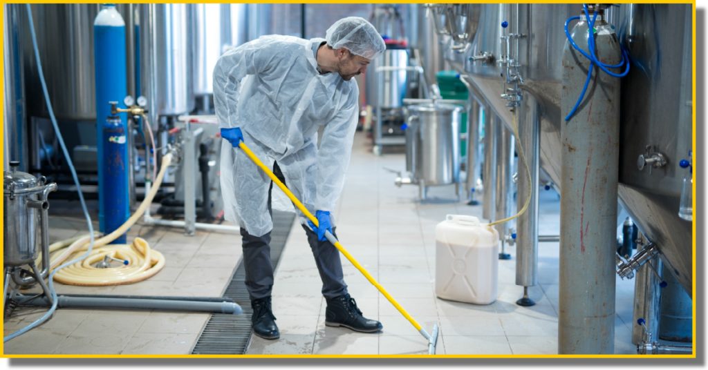A man in a white coat is cleaning equipment inside a food production facility