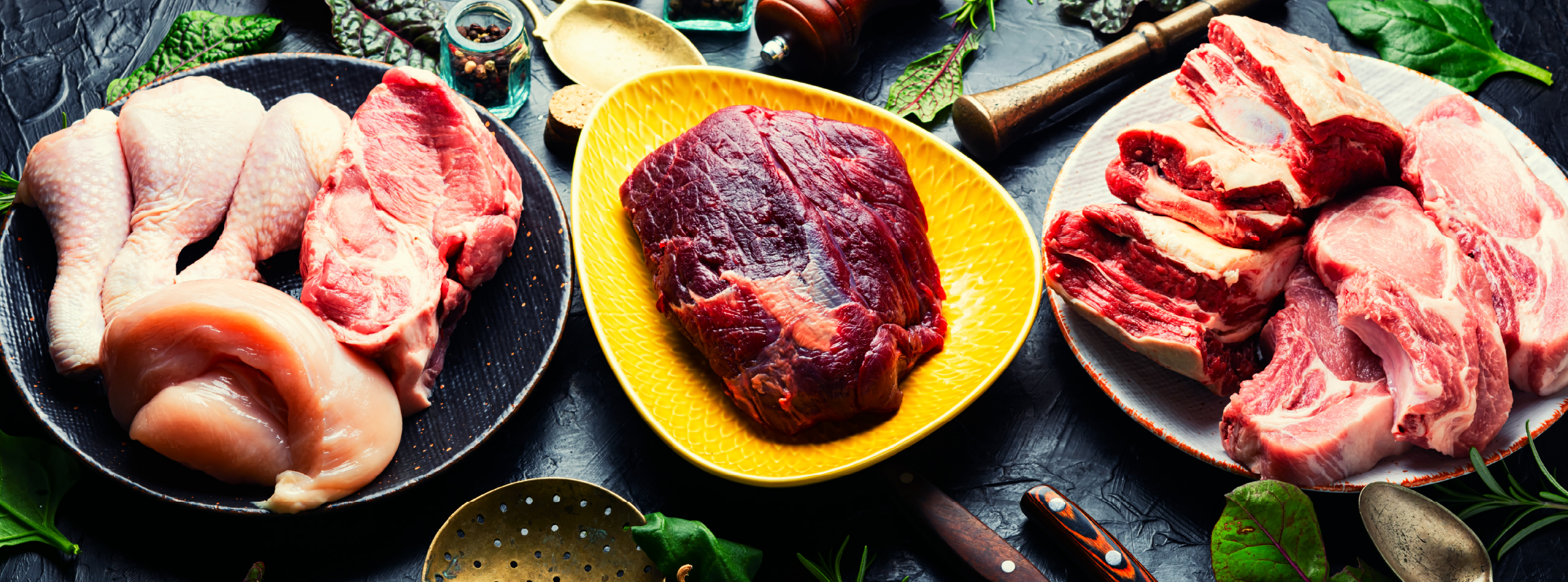 Raw meat, including chicken, beef and lamb, arranged on plates surrounded by herbs, spices and utensils