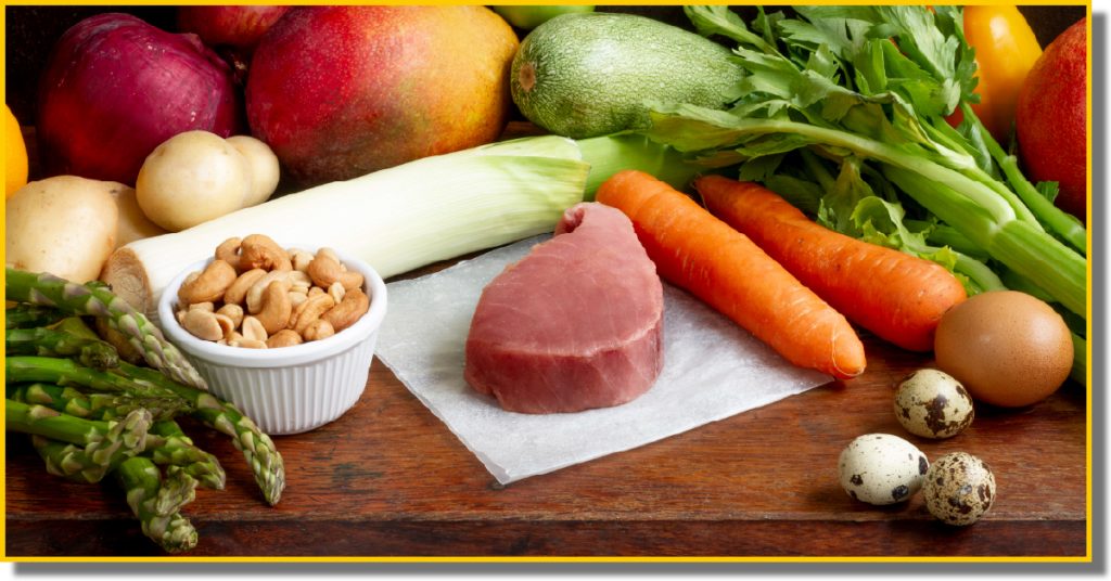 A colourful assortment of fresh vegetables and cooked meat arranged on a wooden table.