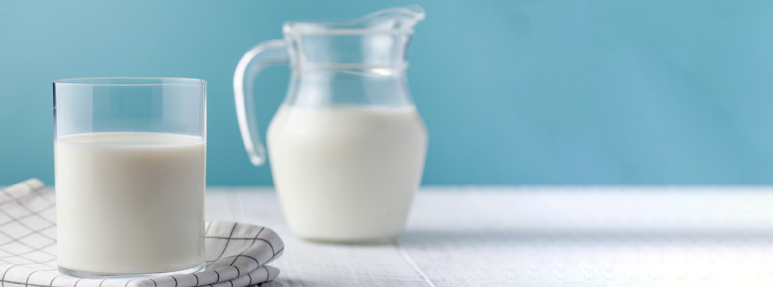 A glass of milk sits next to a pitcher of milk on a wooden table