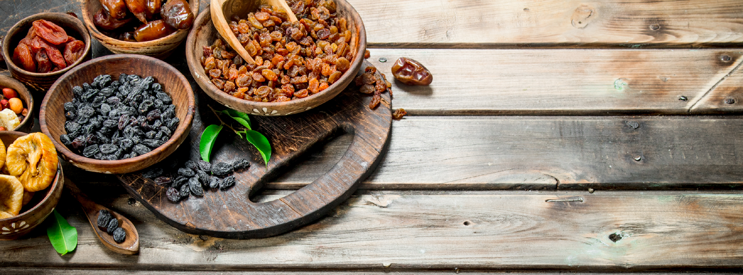 A variety of dried fruits and nuts arranged in wooden bowls on a rustic wooden table.