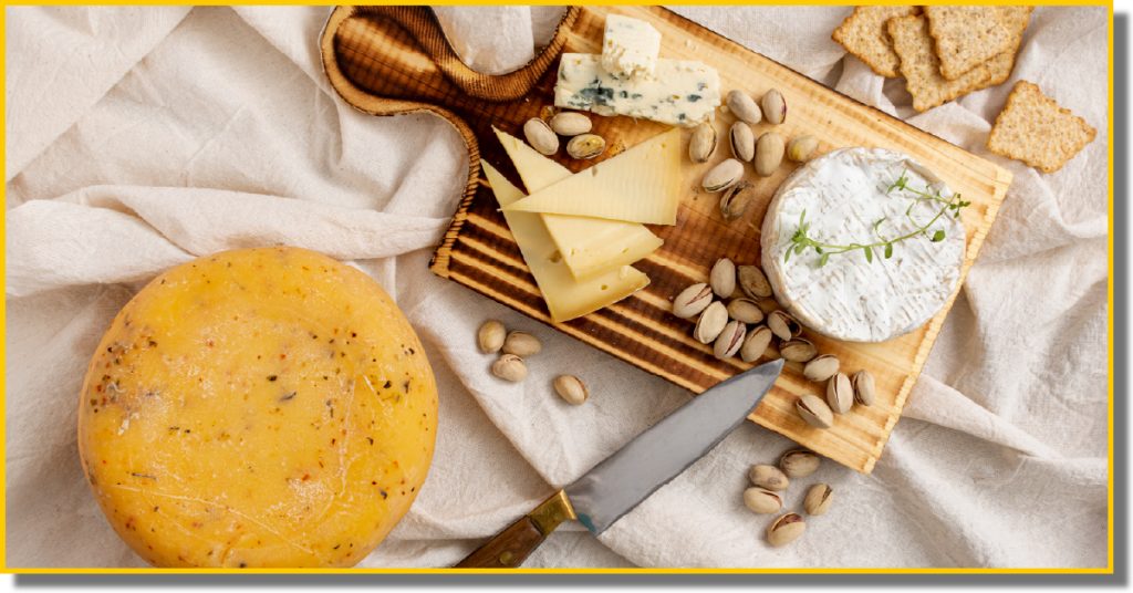 A wooden cutting board displays an assortment of cheese, nuts, and crackers arranged artfully