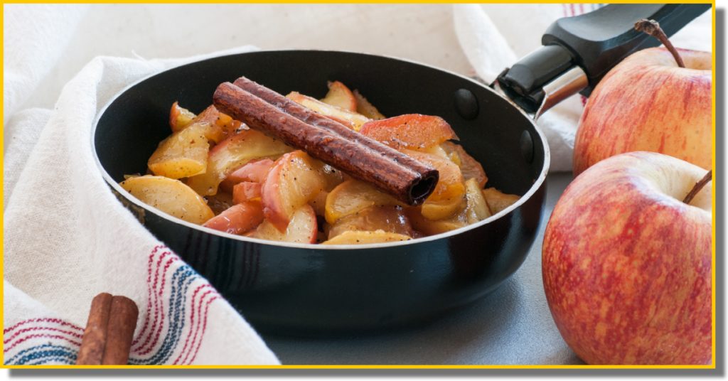 A bowl of apple cinnamon sauce, rich in color, with visible apple chunks and a stick of cinnamon on top