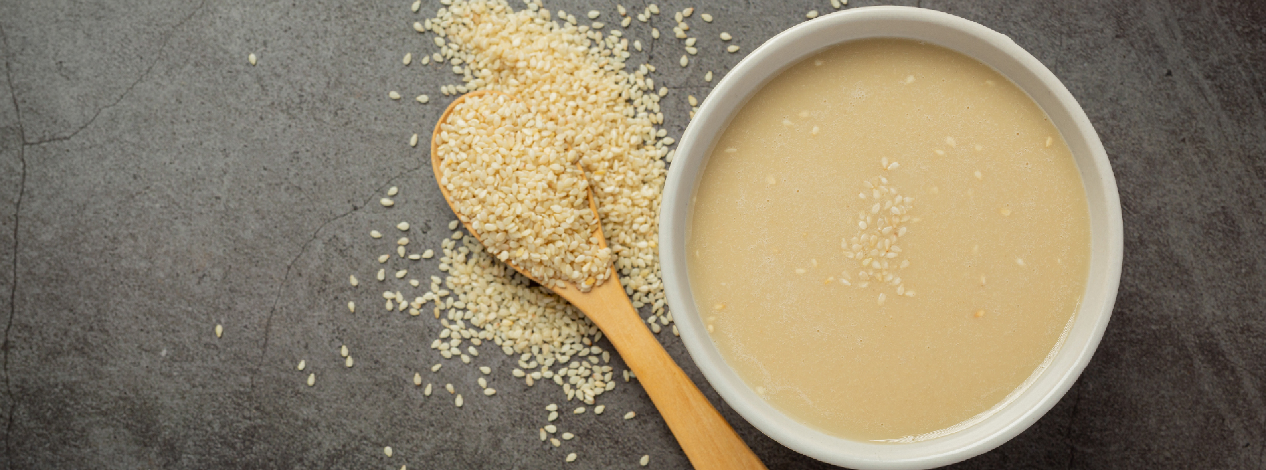 A bowl of sesame paste with a wooden spoon resting inside, showcasing its creamy texture and rich colour