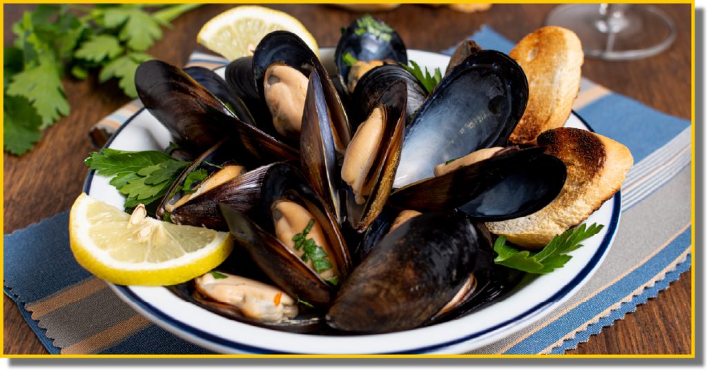 A white bowl filled with mussels, accompanied by a fresh slice of lemon on the side.