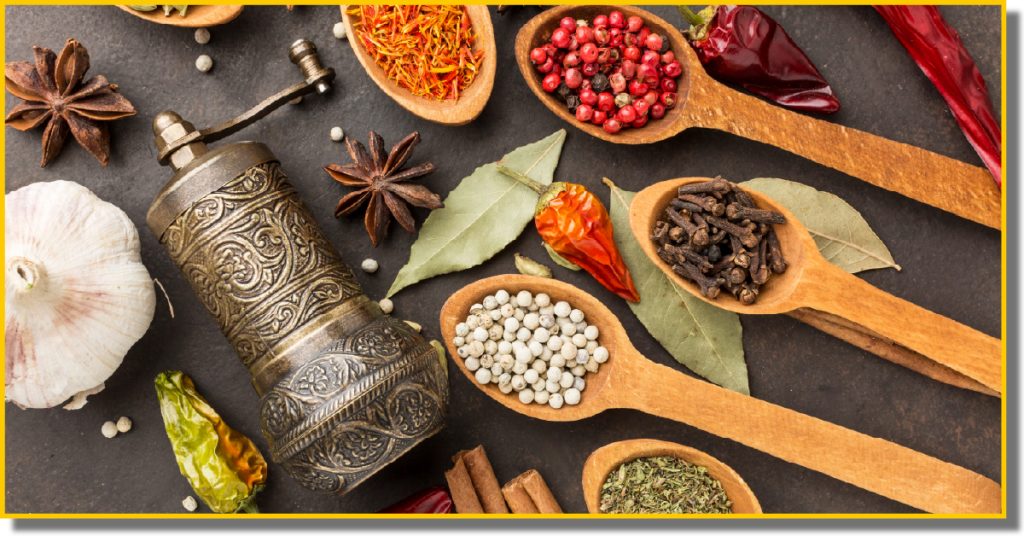 A collection of colourful spices and herbs displayed in wooden spoons on a rustic surface.