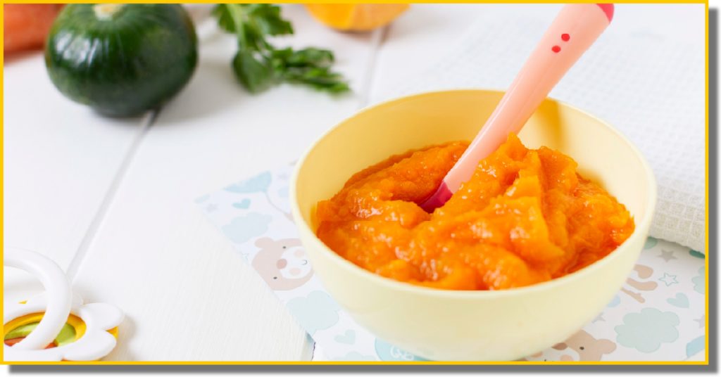 A bowl of smooth orange baby food with a small spoon resting inside it.