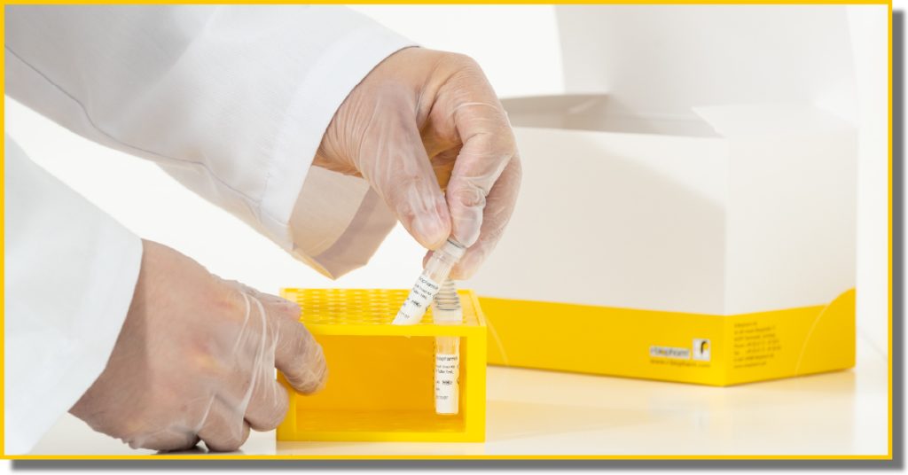 A person in a white coat holds a yellow box, standing against a neutral background.