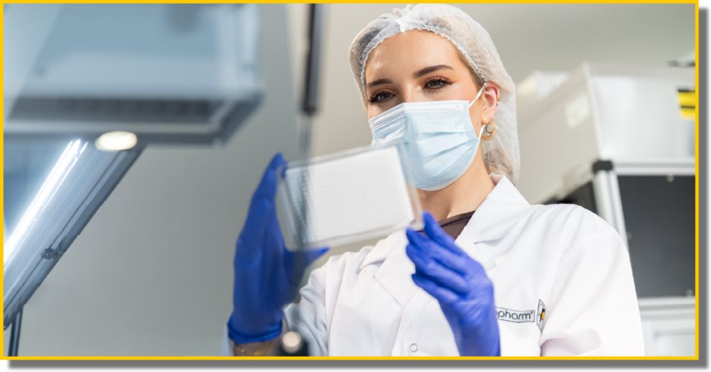 A woman in a lab coat and gloves holds a plastic tray used for diagnostic testing