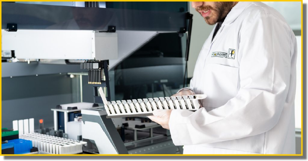 a man in a white lab coat holds a tray of tubes preparing to place it into a machine